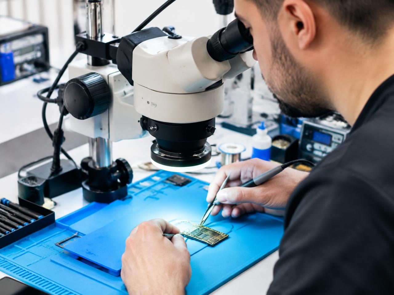 Técnico microsoldando la placa base de un móvil bajo un microscopio